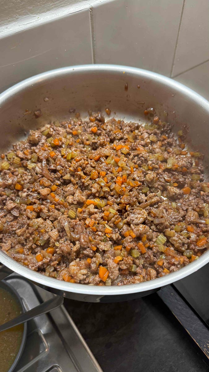 Déglacer avec le vin rouge et ajouter le concentré de tomate.
Gratter les sucs dans le fond de la sauteuse.