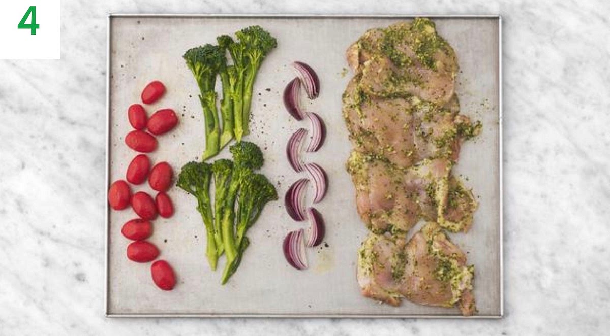 In a medium bowl, combine the chicken thighs and pesto. Season with salt and pepper and toss to coat the chicken. Add the chicken thighs to the other side of the baking tray.