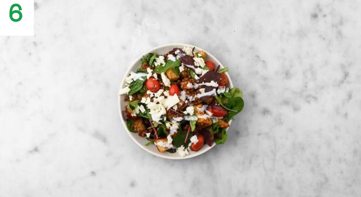 Just before serving, mix the baby leaves and croutons into your salad, then share between your bowls.
Crumble the Greek style salad cheese over the top and drizzle over the yoghurt.