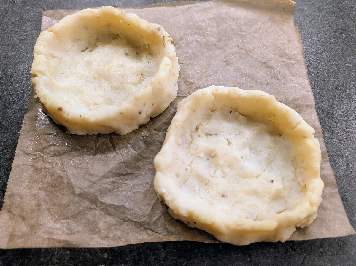 Divide the mix in 4 equal parts, wet your hands, make balls, then flatten them over parchment paper to make patties about 1cm in thickness. Then pinch the mash from the middle outwards, leaving about 1/2cm edge all around, and a thin base, forming the nests. The nest "walls need to be high enough to hold the raw egg without spilling over the edge.