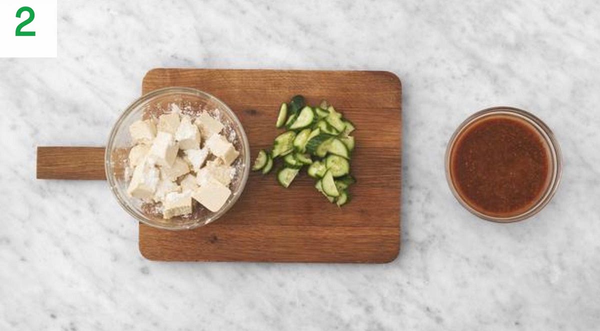 Meanwhile, drain the tofu and throughly pat dry with kitchen paper. Tear into 3cm chunks.
Add the tofu to a medium bowl with the cornflour.
Season with salt and pepper, then toss to coat.
Trim the cucumber, then halve lengthways. Cut into 1cm thick half moons.
Put the rice vinegar, ginger puree, soy sauce, sweet chilli sauce, peanut butter, honey and water for the sauce into another bowl and mix until well combined. Set aside.