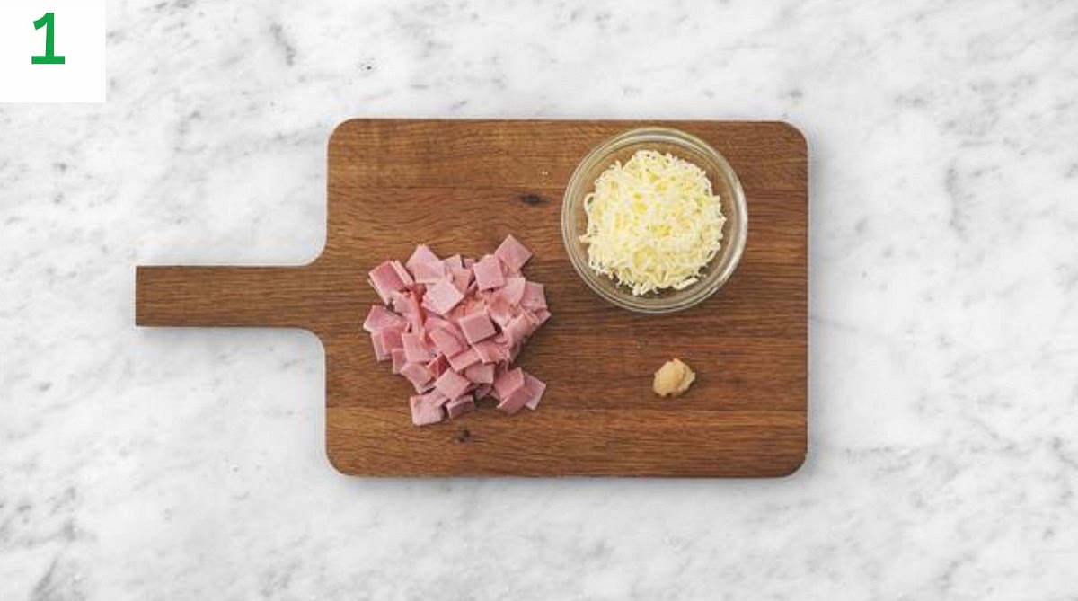Preheat your oven to 240°C/220°C fan/gas mark 9.
Grate the Cheddar cheese.
Peel and grate the garlic (or use a garlic press).
Lay the ham slices on top of each other, then slice into thin strips approximately 2cm wide. Rotate the slices and repeat to create 2cm squares of ham.
