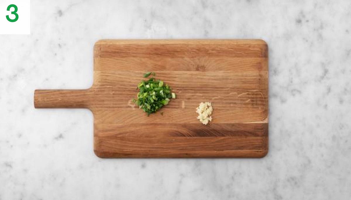 Meanwhile, boil a half-full kettle. Trim and thinly slice the spring onions.
Peel and grate the garlic (or use a garlic press).
Pour the boiled water into a small saucepan with ¼ tsp. Bring back to the boil on high heat and add the peas. Reduce the heat to medium and cook for 2-3 mins.
Drain in a sieve, then pop into a bowl with a drizzle of oil and season with salt and pepper. Cover to keep warm.