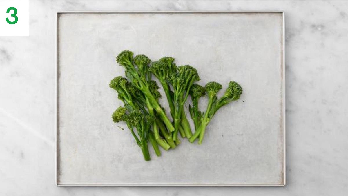 Meanwhile, halve any thick broccoli stems lengthways.
When about 10 mins of roasting time remain, add the Tenderstem® to another baking tray. Drizzle with oil, season, then toss to coat. Spread out in a single layer. tray if necessary.
Roast on the middle shelf for the remaining time until the broccoli is tender and crispy, 8-10 mins.