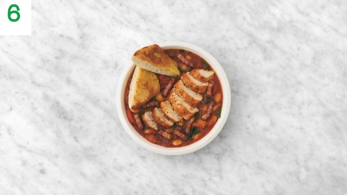 When everything's ready, thinly slice the chicken widthways.
Share the casssoulet style stew between your bowls.
Top with the sliced chicken and serve the garlic ciabatta cut into triangles alongside for dipping and scooping.