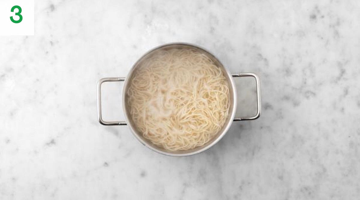Meanwhile, add the noodles to the pan of boiling water and cook until tender, 4 mins.
Once cooked, drain in a sieve and run under cold water to stop them sticking together.
Next, halve the green pepper and discard the core and seeds. Slice into 1cm thick strips.