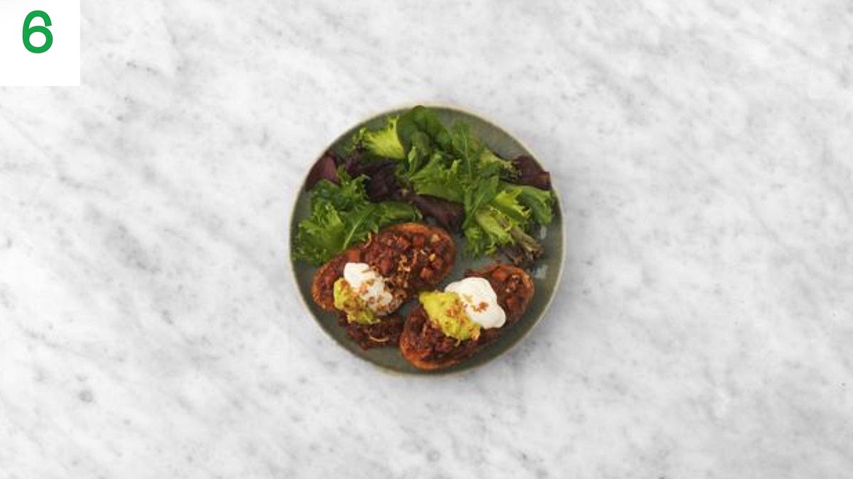 Share your jacket potatoes between your plates and top with the Cajun beef mince.
Finish with a dollop of soured cream, the smashed avocado and a sprinkle of crispy onions.
Serve the baby leaves alongside finished with a drizzle of oil.
