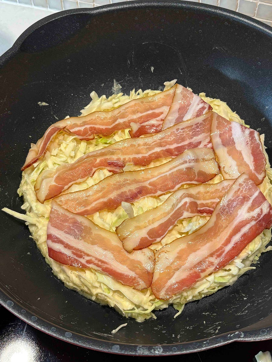 Heat a griddle or pan to about 200°C. Lightly oil it. Pour batter to make ~15 cm pancake. Put bacon on top. Cook for about 5-8 minutes, depending on your pan and stove.
