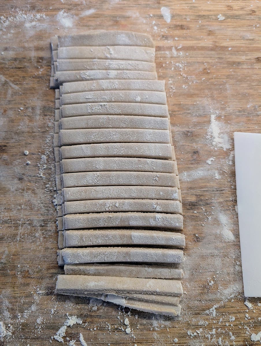 It’s easier to do this step with smaller bits of pasta at a time. On a floured surface, roll the dough with a rolling pin until you have a sheet about 2-3mm thick. Slice the dough in 10 cm strips, flour top and bottom, pile 3 or 4 strips on top of each other, then slice them in 6mm strips. Repeat the process for the rest of the dough.