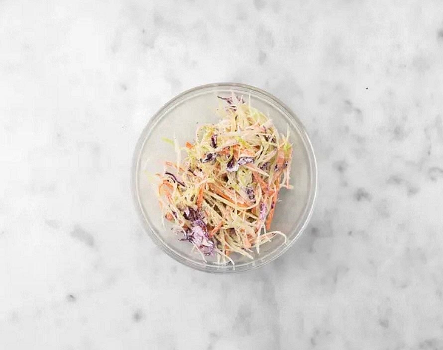Meanwhile, zest, then juice half the lime. Cut any remaining lime into wedges. To a large bowl, add mayo, lime juice, half the lime zest, 1/2 tsp (1 tsp) sugar and 1 tbsp (2 tbsp) oil. Season with salt and pepper, then whisk to combine.
To the dressing, add coleslaw cabbage mix. Toss to coat.