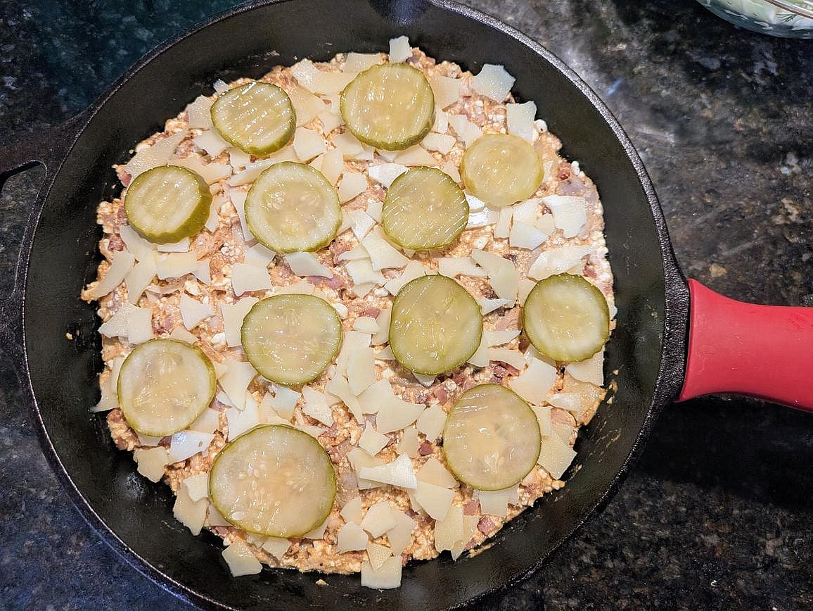 Add your mixture to the cast iron pan. Top with the rest of your Swiss and sliced pickles