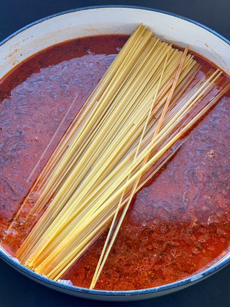 Voeg de ongekookte spaghetti toe. Laat de pasta ongeveer 12 minuten zachtjes koken zonder deksel. Roer regelmatig door zodat de spaghetti niet aankoekt. Vooral tijdens de eerste 5 minuten is goed roeren belangrijk.
TIP: de pasta moet te niet hard koken, anders verdampt het vocht maar wordt de pasta niet gaar. De saus moet ook niet te zacht pruttelen, anders wordt je pasta ook niet gaar en dikt de saus niet in. Zachtjes koken is echt belangrijk. Je krijgt vanzelf daar gevoel in.