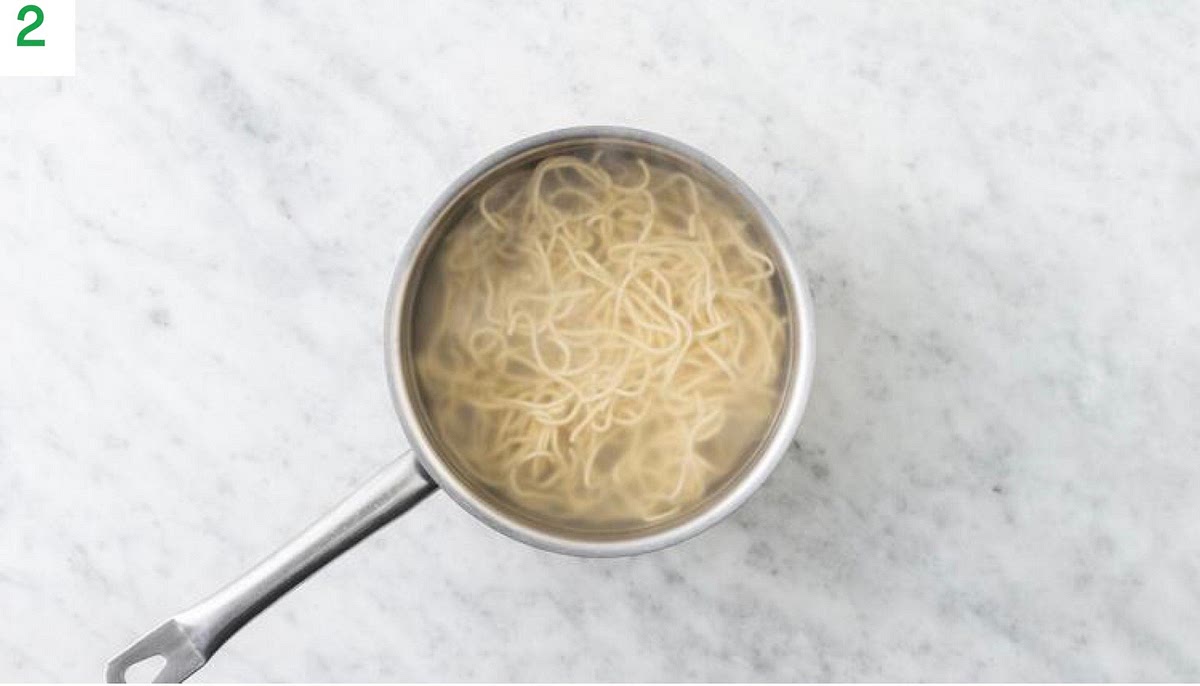 Meanwhile, pour the boiled water into a medium saucepan with ½ tsp salt and bring to the boil.
Add the noodles and cook, 4 mins.
Once cooked, drain in a sieve.
Crush the peanuts in the unopened sachet using a rolling pin.