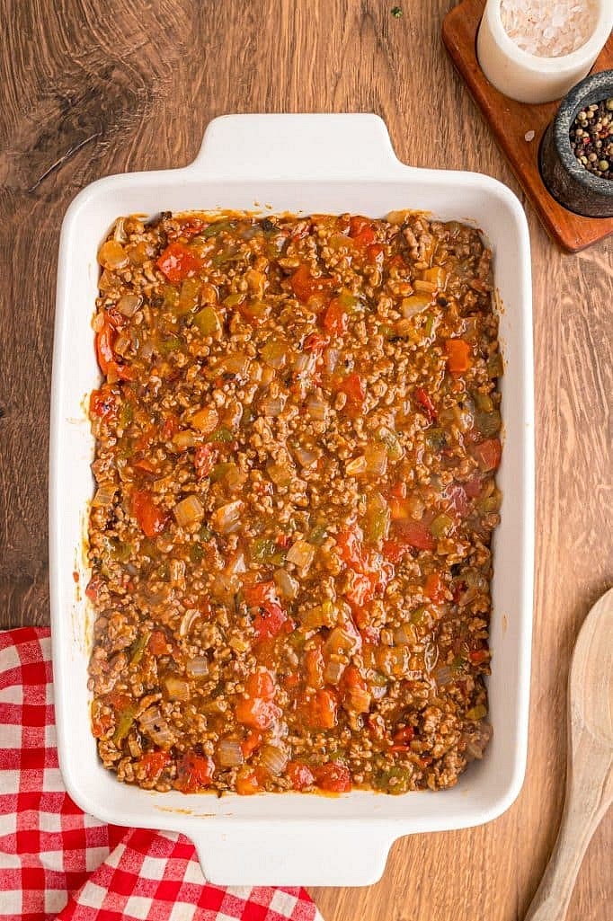 Spread the beef mixture evenly over the partially baked biscuit layer in the casserole dish.