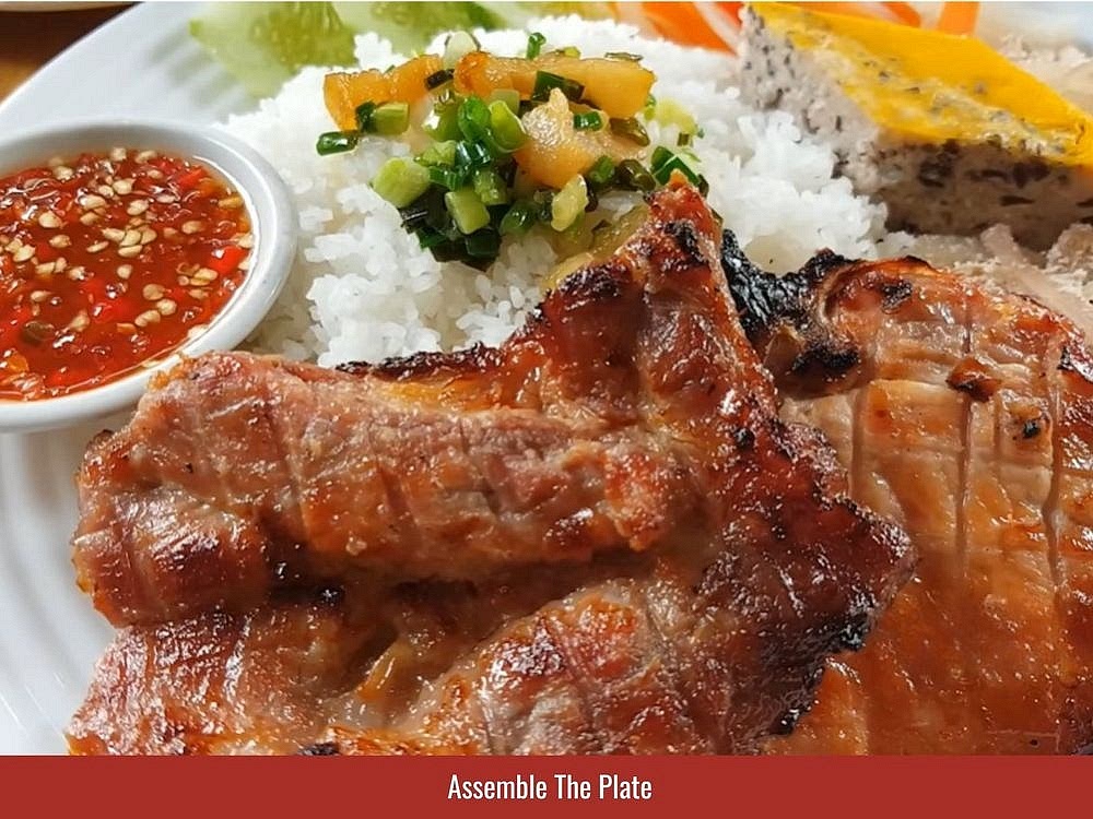 Assemble The Plate
Scoop the broken rice onto a plate and slice the grilled pork into bite-sized pieces. Set the pork chops (sườn), a slice of egg meatloaf (chả), and a mound of pork skin (bì) alongside the rice, with pickled vegetables if you're using them. Spoon the pork fat that mixes with scallions (tóp mỡ hành) over the rice. Serve the drizzling sauce (nước mắm) on the side, with extra chopped chili for anyone who wants more heat.