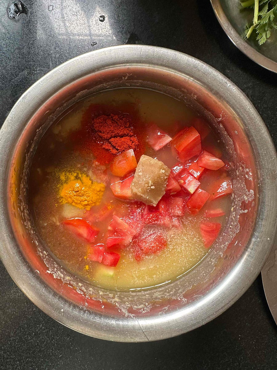 Take a kadhai, and don’t yet switch on the flame. Add the boiled and mashed arhar dal to the kadhai. Add chopped tomatoes, imli juice, jaggery, red chilli powder, haldi. Add salt and hing to taste.