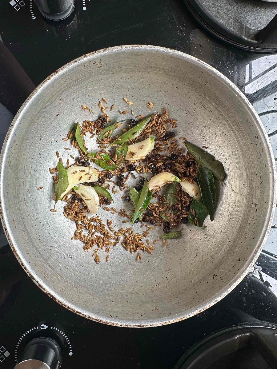 Dry roast cumin seeds, pepper corns, garlic cloves, and curry leaves till it browns slightly. Then add half spoon oil, and fry the ingredients for 30 seconds on very low flame. Be careful that the mix does not burn.
