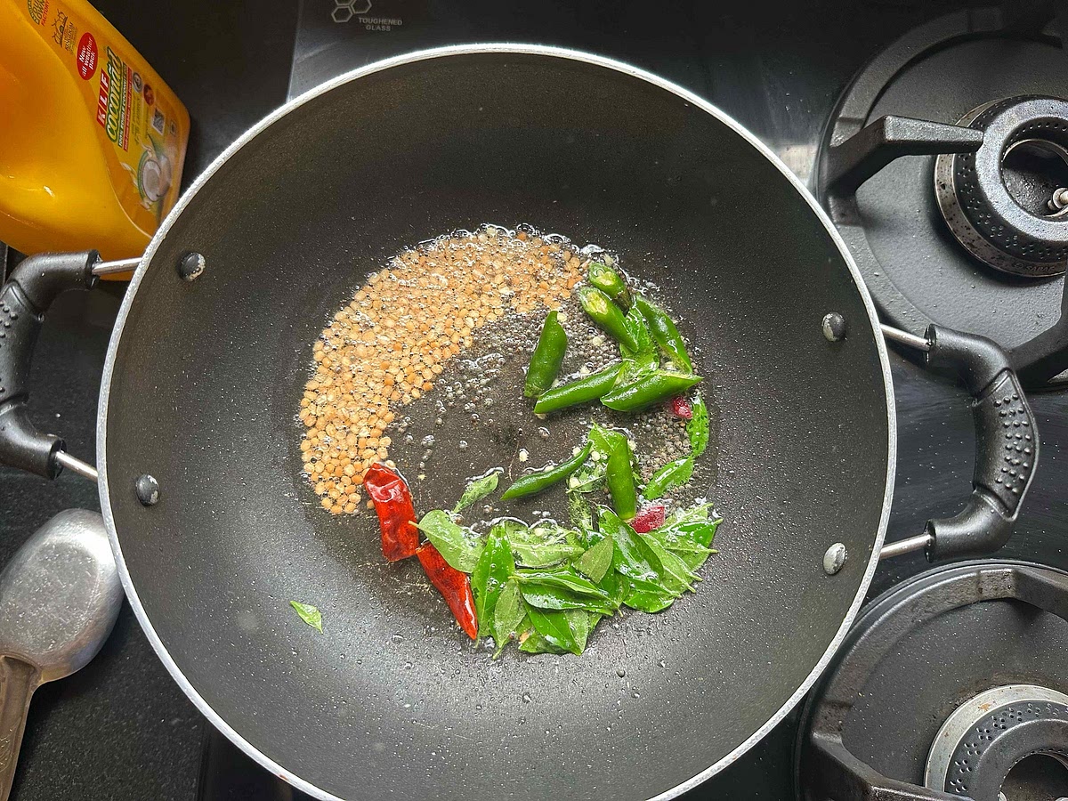 After the mustard seeds begin to cackle, add green chillies, curry leaves and dried red chilies.