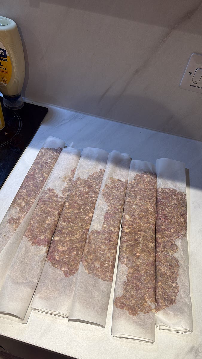 Using the bottom sheet of baking paper, roll the flattened meat from one side to the other, creating a long roll. Repeat with the remaining mixture. You should get several long rolls from the 1kg of meat.