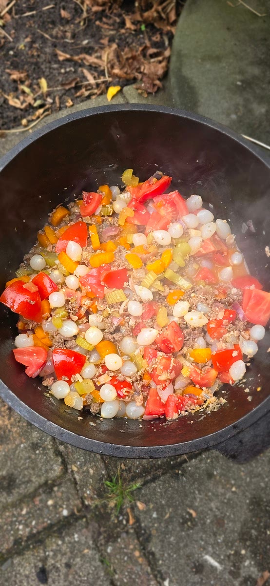 Snijd de tomaten in blokjes en voeg ze toe. Voeg ook de BBQ-saus, de suiker, de in ringetjes gesneden chilipepers en de uitgelekte zilveruitjes toe. Sluit de pan en laat alles met 8 briketten onder de Dutch Oven en 12 briketten op het deksel ongeveer 1 uur sudderen.