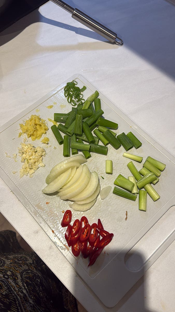 Finely chop the garlic, grate the ginger and slice the white onion. Cut most of the spring onions into chunky pieces, reserving some of the green tops for later. Slice your red chillies.