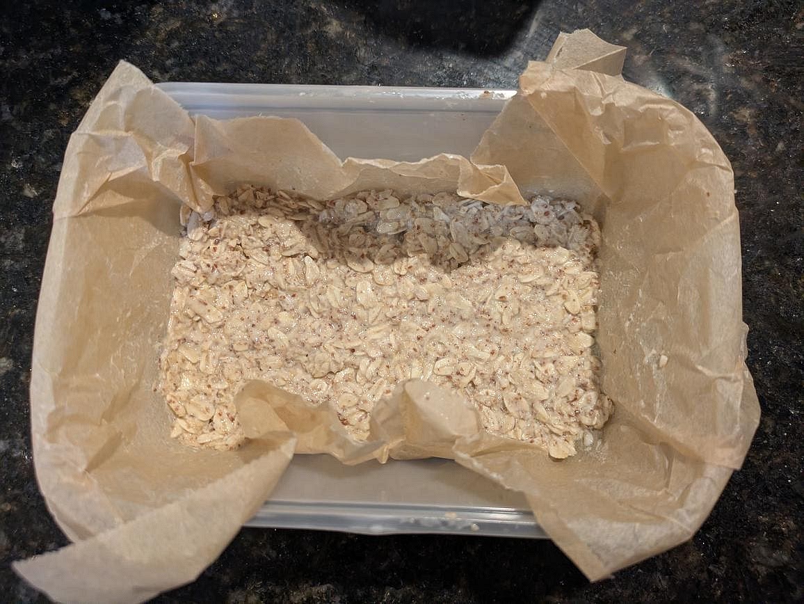 In a lined 9" square baking pan, spread 2/3 of the oat mixture (~300 g). Wearing kitchen gloves to prevent sticking, flatten to an even thickness.