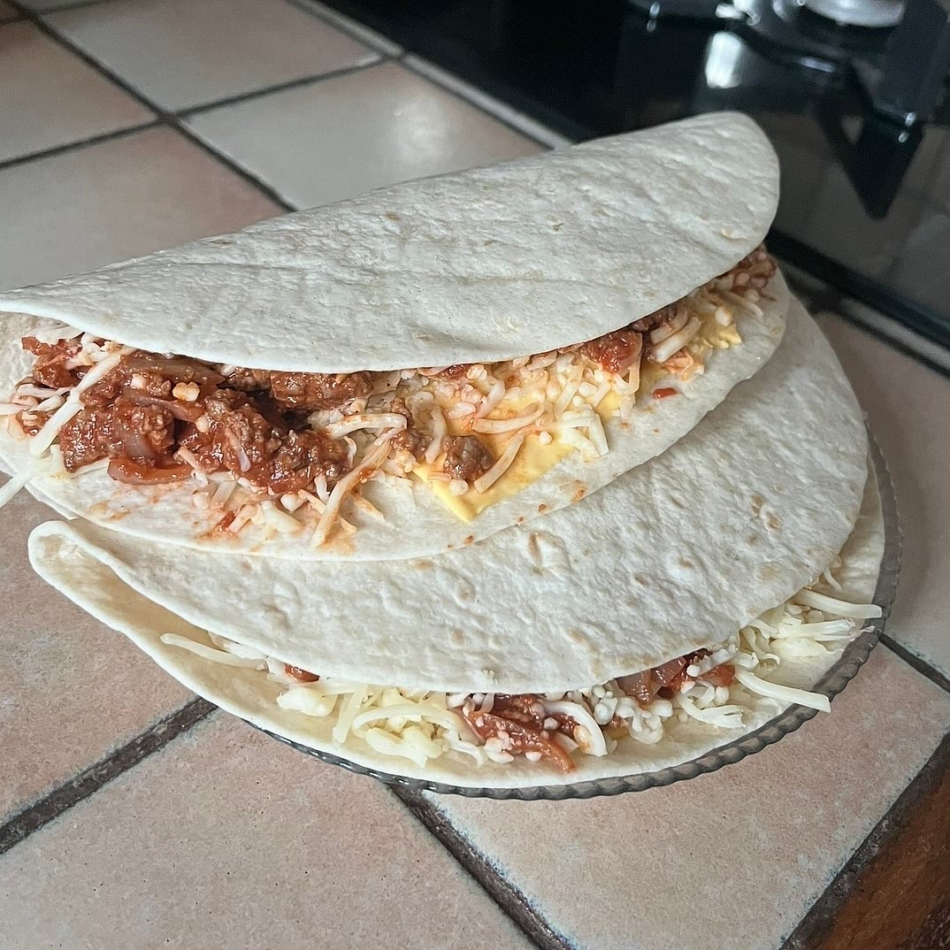Take a plate and put the tortilla on it.
Put on one half the cheese, the meat, and more cheese on top.
Then fold it in half