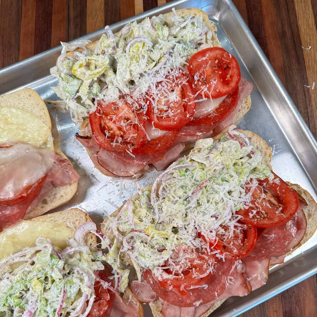 Once the cheese is melted and the sandwiches are hot, top them with more Parmesan cheese. Add slices of tomato that have been seasoned with salt and pepper. Top sandwiches with the grinder salad mixture. Enjoy!