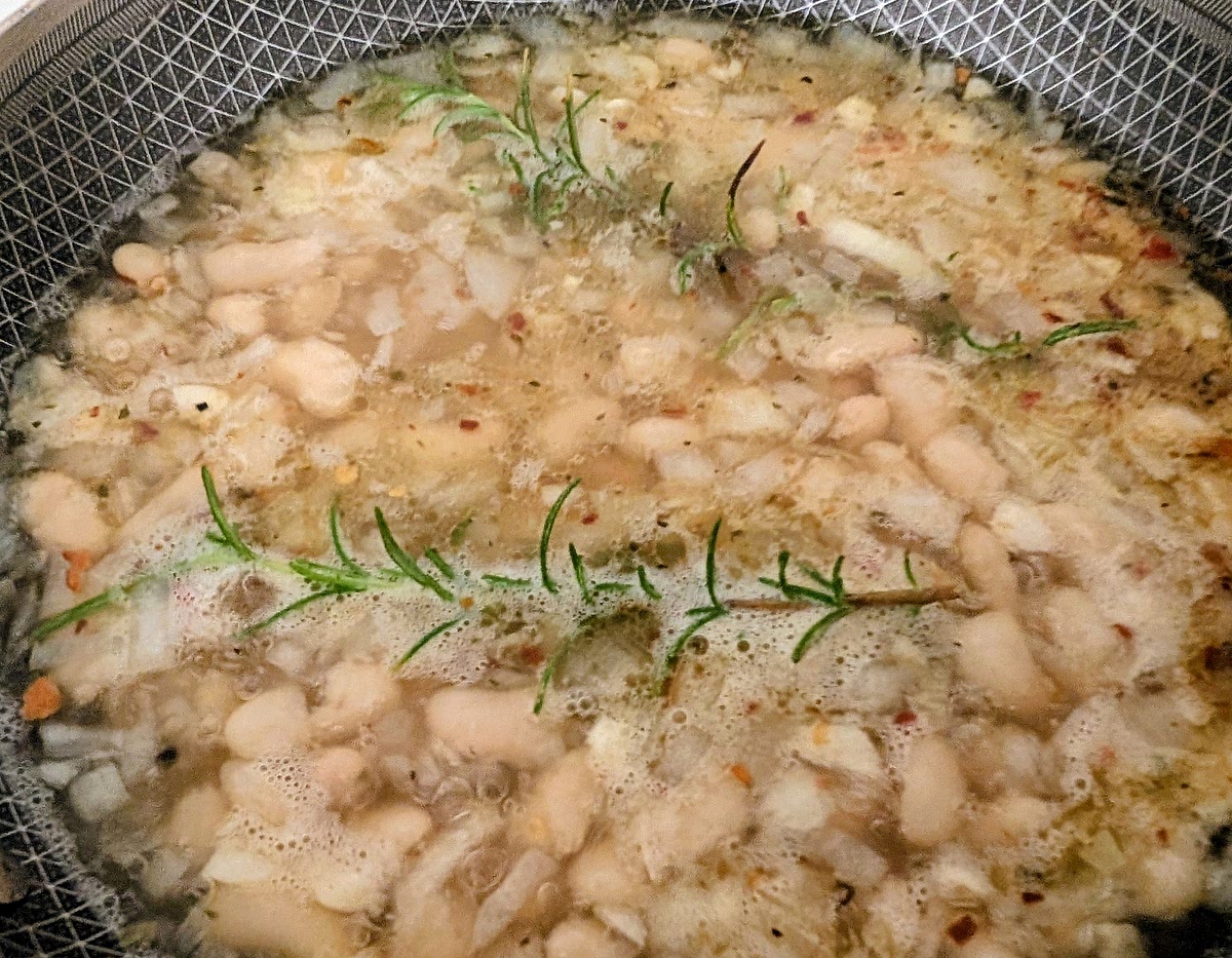 Add the vegetable stock, the rinsed beans, the thyme leaves, 2 sprigs of rosemary, the crushed chillies (optional) and a freshly ground toasted black pepper to taste. Stir it well, bring it to a boil, then reduce heat to low and cover with a lid, and simmer it for 10-12 minutes.