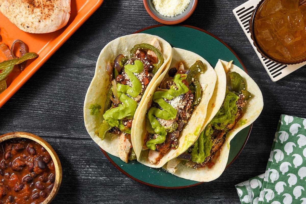 Assemble your balanced dinner Warm the gluten-free corn tortillas in a dry frying pan for approximately 20–30 seconds per side, until flexible. Divide the fajita chicken and roasted peppers between four tortillas, giving each person two. Add a little black bean filling and drizzle with avocado-lime crema. Serve the remaining black beans and fresh rainbow salad alongside. Finish with fresh lime wedges.